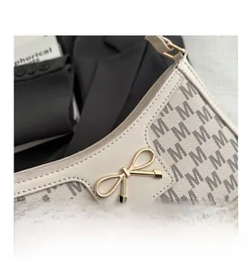 Detail der beigen Schultertasche mit goldener Schleifenschnalle und M-Muster-Leder