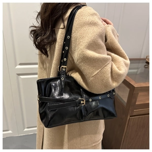 Detail of black oil-wax leather shoulder bag with golden metal grommets on strap