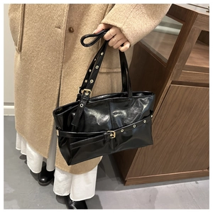 Detail of glossy black oil wax leather tote bag with metal buckles and eyelet accents