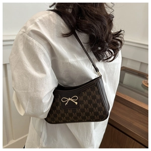 Detail der dunkelbraunen Baguette-Tasche mit Monogramm und goldenem Schleifendekor