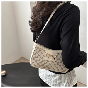 Detail der cremefarbenen Baguette-Tasche mit M-Print und goldener Schleifenschnalle