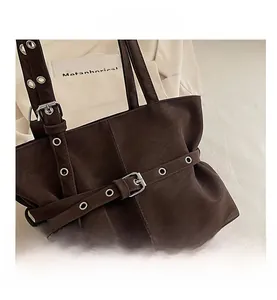 Detail of dark brown suede tote bag featuring metallic eyelets and buckle strap design