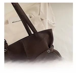 Detailed close-up of dark brown suede tote bag featuring metallic eyelet belt buckle strap