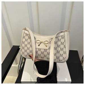Detail der cremefarbenen Schultertasche mit grauem M-Monogramm und goldener Schleife