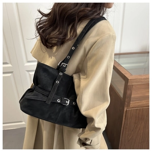 Detail of black matte shoulder bag with silver eyelets and buckle straps on a model