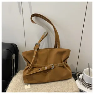 Detailed view of brown faux suede tote bag with silver buckle strap on a cozy cushion
