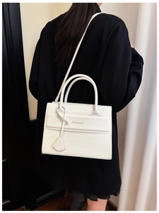 Détail du sac à main blanc à texture crocodile avec texte porté sur un blazer noir chic