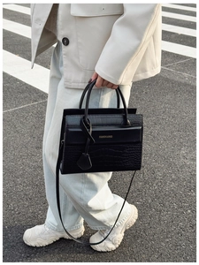 Détail d'un sac à main noir en cuir motif crocodile avec texte doré et fond urbain chic