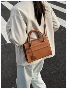 Détail d'un sac à main marron avec motif crocodile, logo en métal et poignée chic
