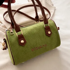 Détail du sac polochon en daim vert avec poignées en cuir marron et boucles dorées