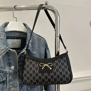 Borsa a spalla baguette con stampa M e fiocco dorato esposta su una giacca di jeans