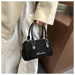 Gros plan du sac cylindre en daim noir avec logo M'DoLnu blanc et zip doré élégant