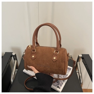 Gros plan du sac Boston en daim marron avec logo embossé et ferrures en métal doré