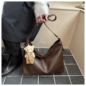 Dettaglio della borsa tote in pelle marrone scuro con tracolla e ciondolo a orsetto