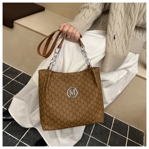 Close-up of brown tote bag with M-pattern print and metallic chain strap detail