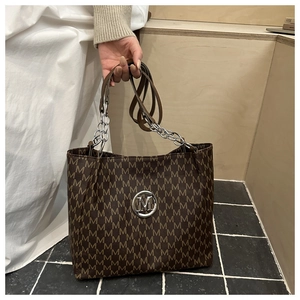 Detail shot of brown monogram tote bag featuring a metallic M logo and chain strap