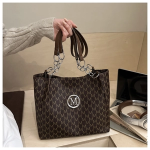 Detail of vintage brown tote bag with M-pattern and silver chain strap in daily life scene