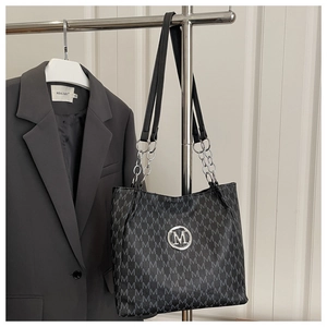 Detail of black leather tote bag featuring monogram M print and silver chain strap