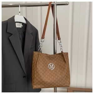 Macro detail of brown tote bag featuring logo print texture and silver metallic M buckle