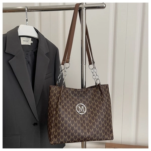 Close-up of brown faux leather tote with M-pattern and chain strap on grey blazer