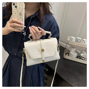 Detail of white PU leather crossbody bag with gold cylindrical clasp on denim jacket
