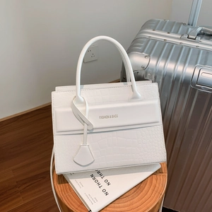 Sac à main blanc en cuir synthétique à motif crocodile sur des livres et valise