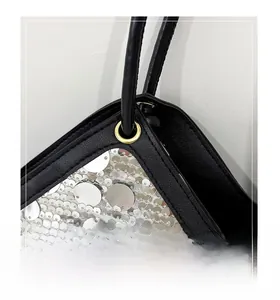 Detail of silver sequins on a black evening bag with golden metal eyelets and handle