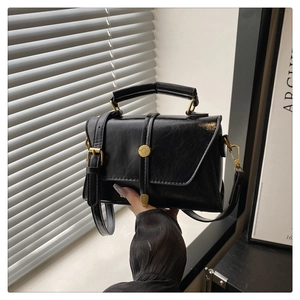 Detail of a vintage black glossy leather handbag with gold circular buckle and top handle