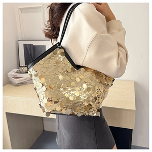 Detail view of gold sequin tote bag with black leather straps worn by a model