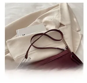 Detail of burgundy suede shoulder bag featuring slim strap and silver rivet accents