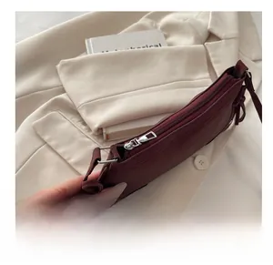 Detail of smooth silver zipper on a burgundy bow shoulder bag over a beige blazer