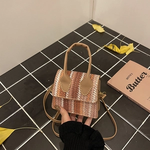 Minimalist linen patchwork straw bag with brown leather handles and a long shoulder strap