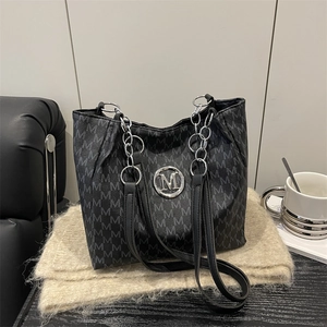 Black large tote bag with M-letter pattern and silver chain on a beige knit rug