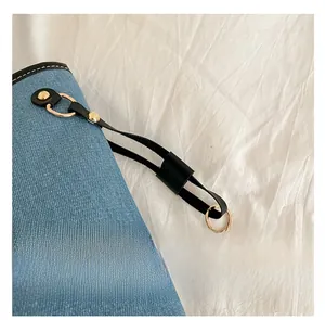 Detail of blue denim tote bag with black leather trim and golden metal hardware studs