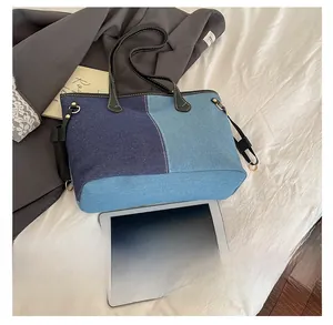 Detail of color-block denim tote bag with leather trim on a minimalist fabric backdrop