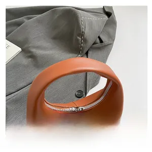 Close-up of brown leather handbag featuring silver double zippers and smooth rounded handle