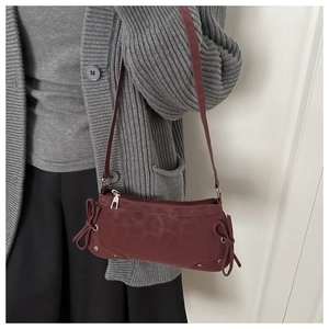 Detail of burgundy underarm bag with leopard texture, side bows and silver metal studs
