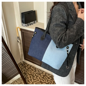 Detail of color-block denim tote bag with black shoulder straps and contrast stitching