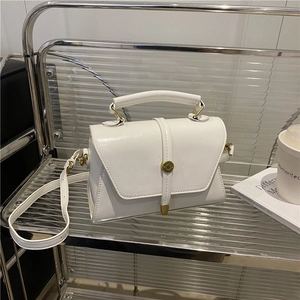 Witte glanzende leren crossbodytas met handvat en gouden sluiting op een standaard