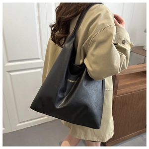Détail du grand sac cabas en cuir noir avec lettrage doré sur un modèle en trench