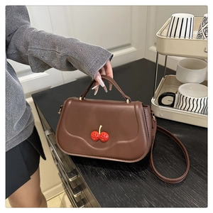 Detailed view of a brown vintage leather handbag featuring a red cherry decoration