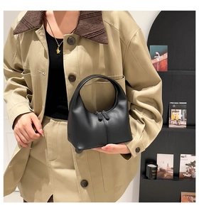 Detail of a minimalist black matte leather handbag featuring dual zippers and seamless handle