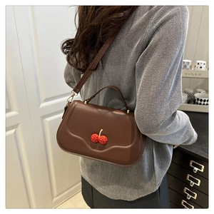 Detail of dark brown leather crossbody bag featuring a 3D cherry ornament on gray sweater