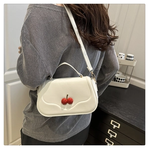 Close-up of white minimalist shoulder bag featuring two red 3D cherry accents on front