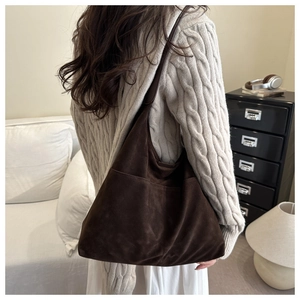 Détail d'un grand sac cabas en daim café avec poche avant porté par un mannequin en pull