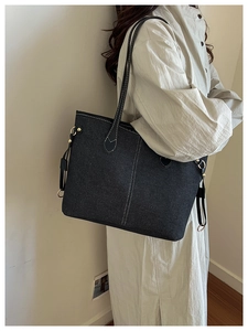 Detail of black denim tote bag with white contrast stitching and gold metal hardware