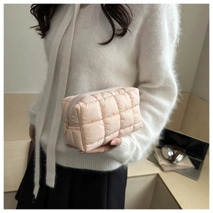 Close-up of pink quilted puffer cosmetic bag held by a person in a minimalist setting