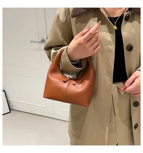 Close-up of a brown leather crescent handbag held by a model in a minimalist setting
