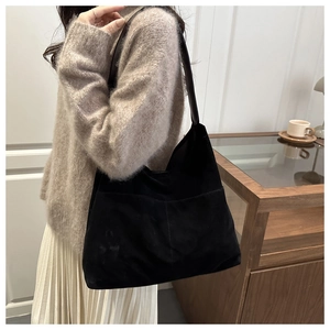Détail d'un grand sac cabas noir en daim mat avec bandoulière en cuir porté par un mannequin