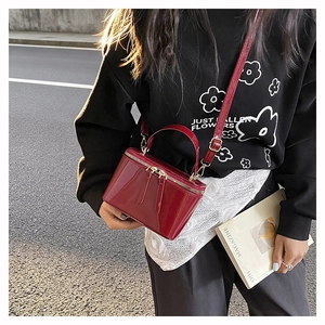 Close-up of a burgundy patent leather mini box bag with gold-tone dual zippers and handle